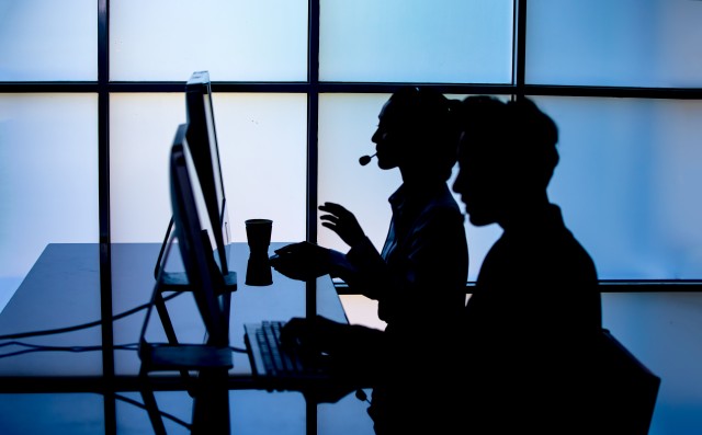 A hacker types on a computer while sitting with a mask, symbolizing the act of impersonating someone to commit an act of social engineering.